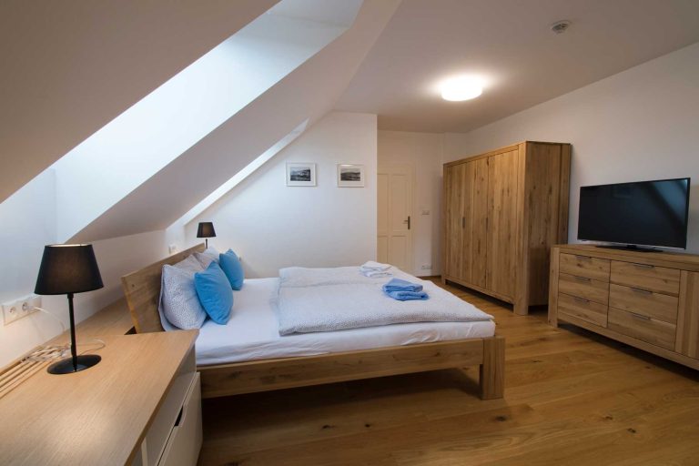 podkrovní ložnice s dvojlůžkovou postelí, dřevěnou skříní a nočními stolky