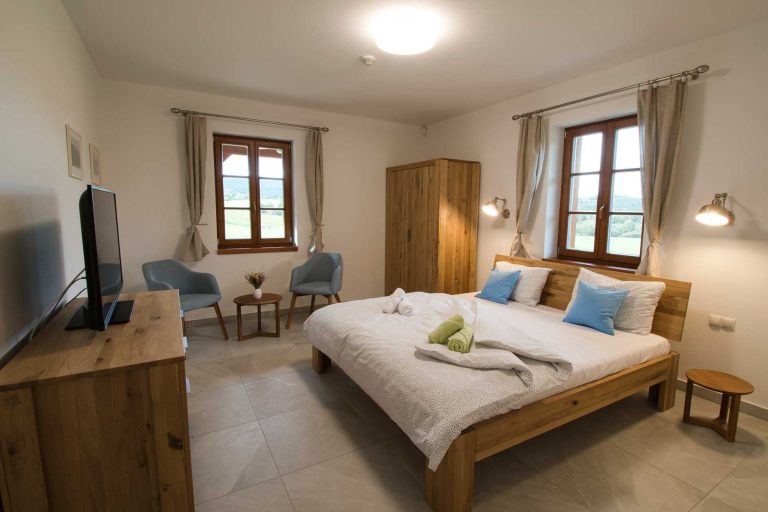 ložnice s manželskou postelí, dřevěnou šatní skříní, dvěma křesly a stolkem