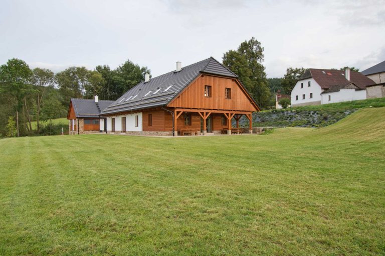 výhled na chalupu obloženou dřevem stojící uprostřed zelené louky